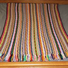 a multicolored blanket laying on top of a bed next to a wooden frame