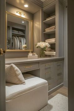 a dressing room with a bench, mirror and closet doors open to reveal an organized closet