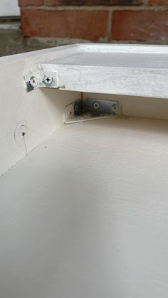 the bottom half of a white cabinet door with two screws on it and a brick wall in the background