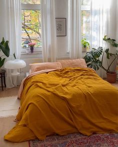 a bedroom with yellow linens and plants in the window sill, along with a rug on the floor