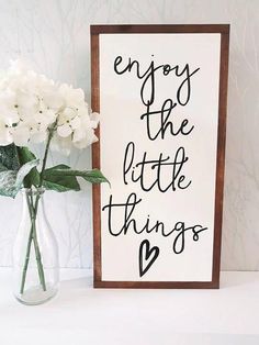 a vase filled with white flowers next to a sign that says enjoy the little things