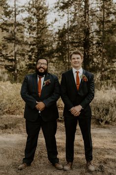 two men standing next to each other in front of some trees and grass with one man wearing an orange tie