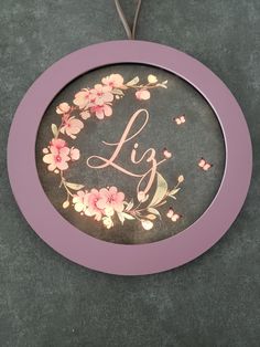 a pink frame with flowers and the word l is hanging on a gray wall next to a pair of scissors