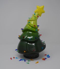 a green ceramic christmas tree with a star on top and confetti all around it