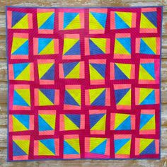 a colorful quilt hanging on the side of a wooden wall with pink, yellow and blue squares