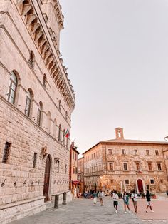 people are walking around in an old town square with stone buildings and cobblestone streets