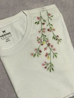 a white t - shirt with flowers embroidered on the front and back, sitting on a gray surface