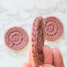 a hand holding a piece of crochet next to two small round objects on a table