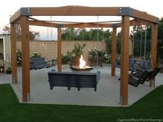 a fire pit in the middle of a backyard with swings and chairs around it,