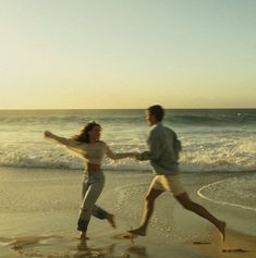 two people running on the beach holding hands