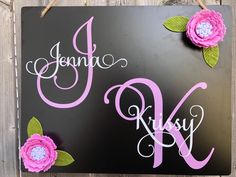 a black sign with pink flowers hanging from it's side on a wooden fence