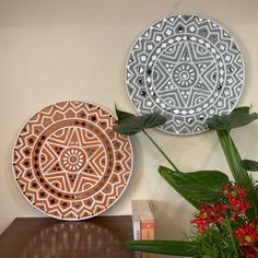 two decorative plates sitting on top of a wooden table next to a potted plant