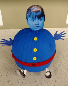 an inflatable blue man sitting on top of a floor next to a wall