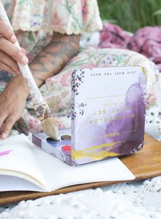 a person sitting on a bed with an open book and paintbrush in their hand