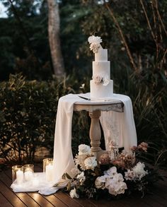 a white wedding cake sitting on top of a wooden table next to candles and flowers