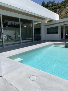 an empty swimming pool in front of a modern house with large glass doors and windows