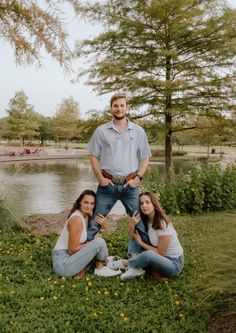 three people are posing for a photo in front of a pond and some trees with yellow flowers