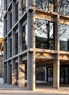 an empty parking lot in front of a tall building with windows on each side and trees growing out of it