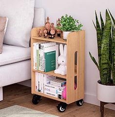 a small wooden book shelf with books and toys on it next to a white couch