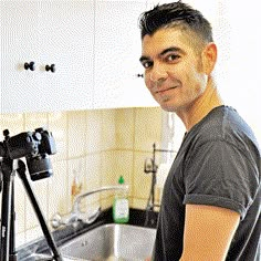 a man standing in front of a kitchen sink with a camera on the counter next to him