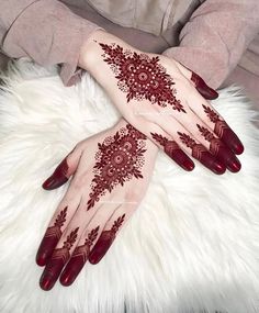 two hands with henna tattoos on them sitting on a white furnishing area