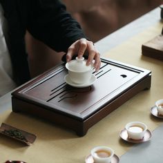 a person pouring tea into a cup on top of a wooden table next to cups and saucers