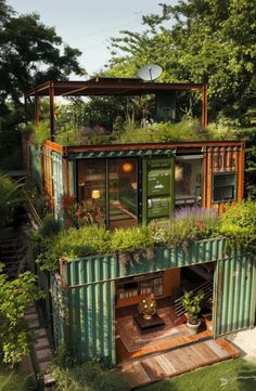 a green shipping container with plants growing on it's roof and stairs leading up to the second floor