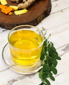 a glass cup filled with green tea next to sliced carrots and ginger on a white table