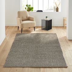 a living room with a chair and rug on the wooden floor next to a window