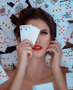 a woman holding four cards in front of her face and surrounded by blue playing cards