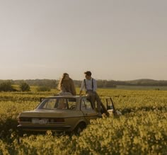 two people are sitting on the hood of a car in a field with yellow flowers