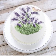 a cake decorated with lavender flowers on a white plate sitting on a wooden table next to a bird