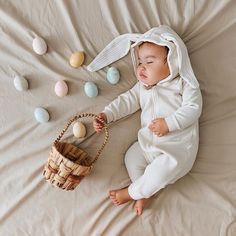 a baby laying on a bed next to an easter basket