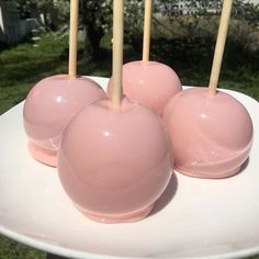 four pink candy apples sitting on top of a white plate with wooden sticks sticking out of them