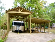 an rv is parked under a covered carport in the driveway next to some trees