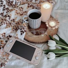 a cup of coffee next to a nintendo wii game controller and some flowers on a table