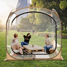 three women sitting in a glass box on the grass