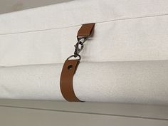 a close up of a white curtain with a brown leather strap hanging from it's end