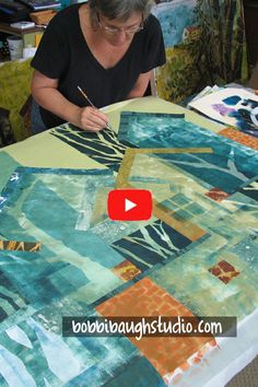 a woman is working on an art project at a table with fabric and scissors in front of her