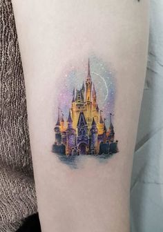 a woman's thigh with a disney castle tattoo on her left leg and fireworks in the sky above it