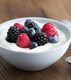 yogurt with berries and blueberries in a white bowl on a wooden table