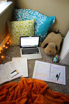 an open laptop computer sitting on top of a desk next to pillows and notebooks