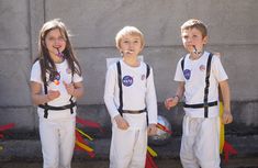 three young children standing next to each other with toothbrushes in their mouths and wearing white outfits