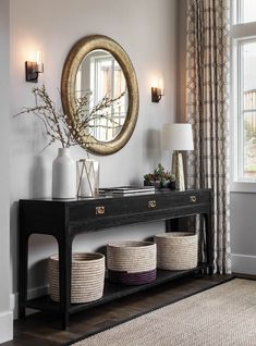 a console table with baskets underneath it and a round mirror on the wall behind it