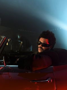 a man sitting in a red sports car with his hand on the steering wheel while wearing sunglasses