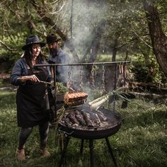 two people standing next to a bbq grill with food cooking on top of it