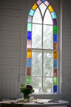 a stained glass window in the corner of a white wall with a bench underneath it