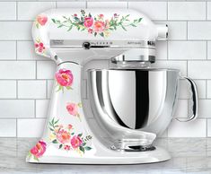 a white mixer with purple flowers on it sitting on top of a counter next to a tiled wall