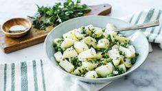 a bowl filled with potatoes and peas on top of a table next to a cutting board