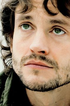 a close up of a man with long hair and green eyes looking at the camera